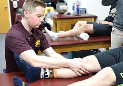 A young man examines the leg of a patient on an exam table.