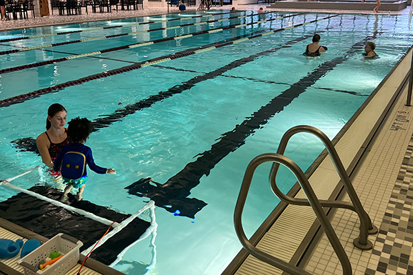An image of the SAC Pool with people swimming, and a swim lesson for a child in the foreground.