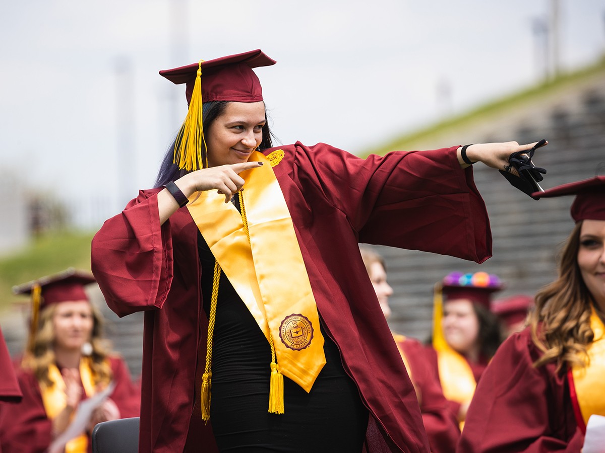 A student smiles and points during spring commencement