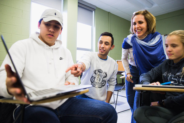 Two CMU students and their instructor looking at something on a laptop in class.