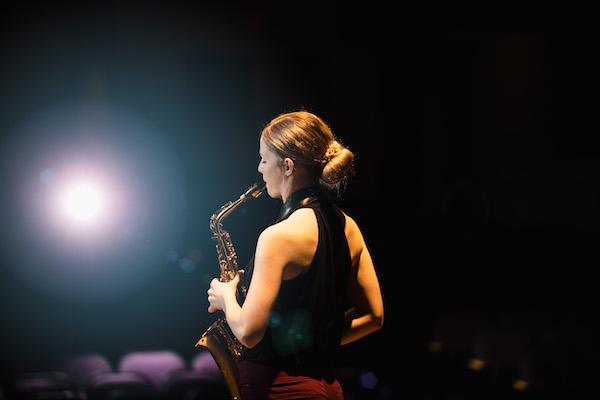 picture of the side of a student on stage in a spotlight playing saxophone 