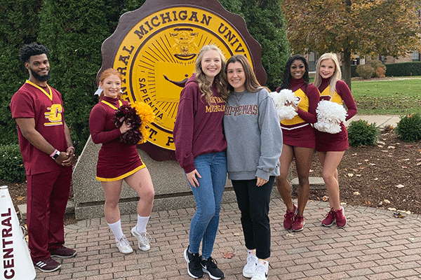 Central Michigan University cheer team members pose in front of the statue of the CMU seal