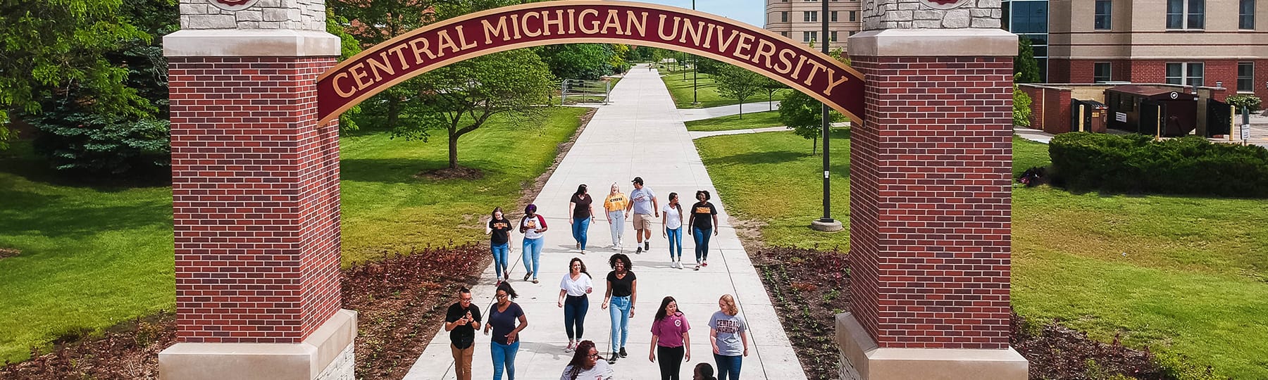 A group of students walks under the Central Michigan University arch on campus during the spring.