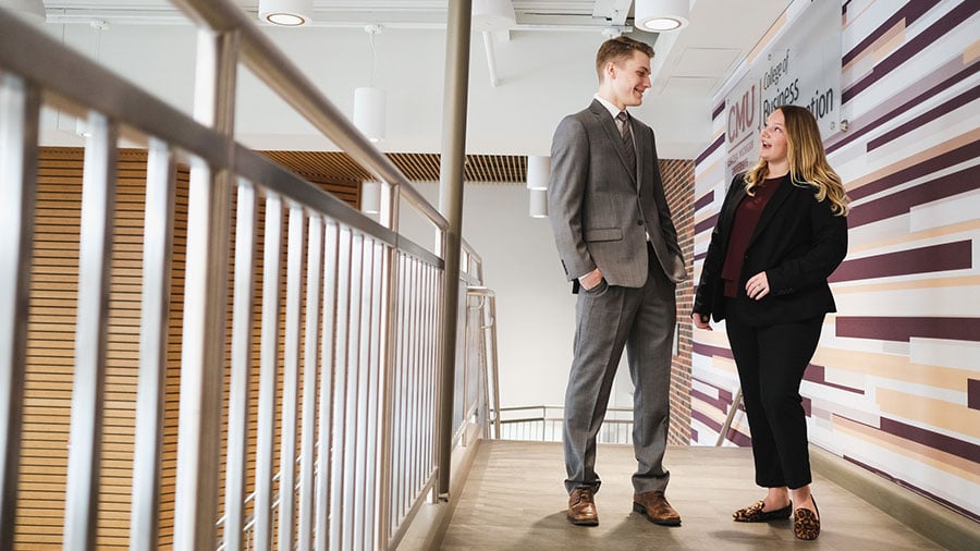 Two students dressed in professional suits talking in a hallway