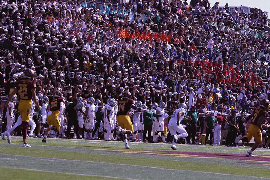 CMU and Eastern football players making a play while the 2023 Band Day students cheer in the stands