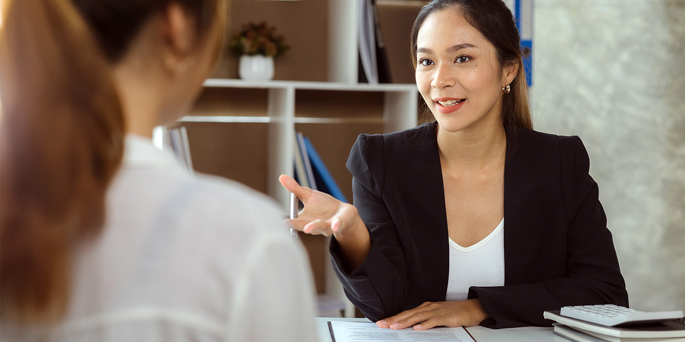 A woman wearing a black blazer talks to a woman in a white blouse.