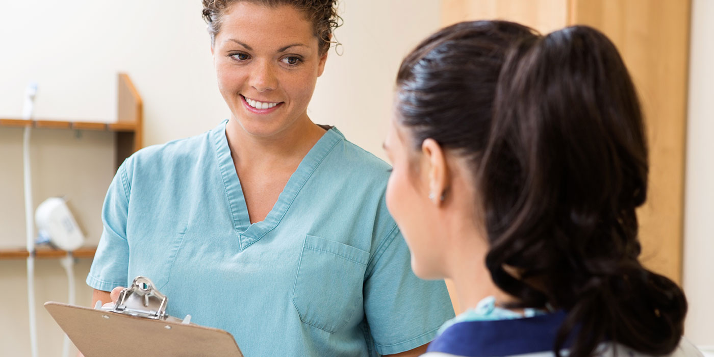 Two women wearing blue scrubs talk to one another.