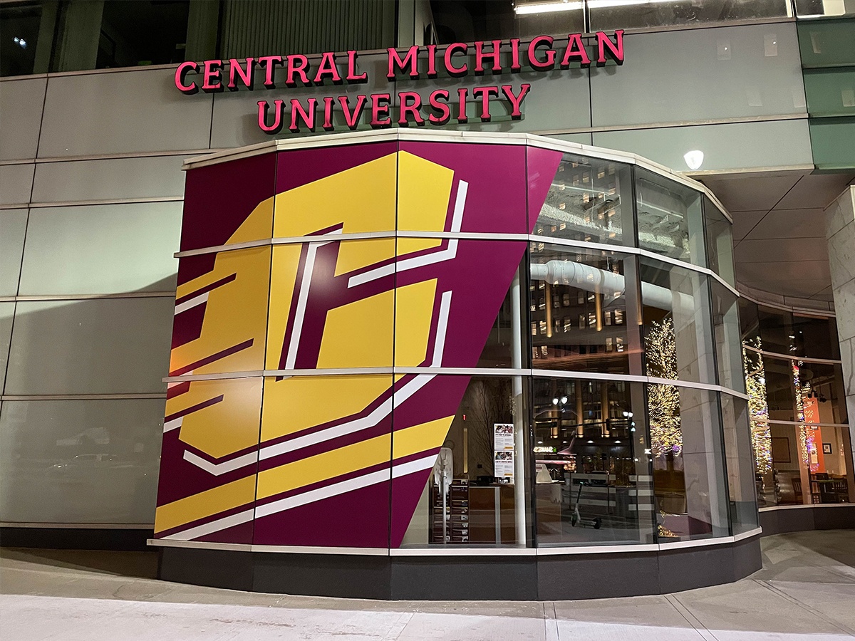 Detroit Center outside of building with glass windows and large action c decal outside as well as light up sign that reads Central Michigan University