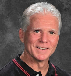 Headshot of Bill Cecil.  The background is brown and he is wearing a black polo with two orange stripes on the collar.  Bill is smiling and has short silver hair.