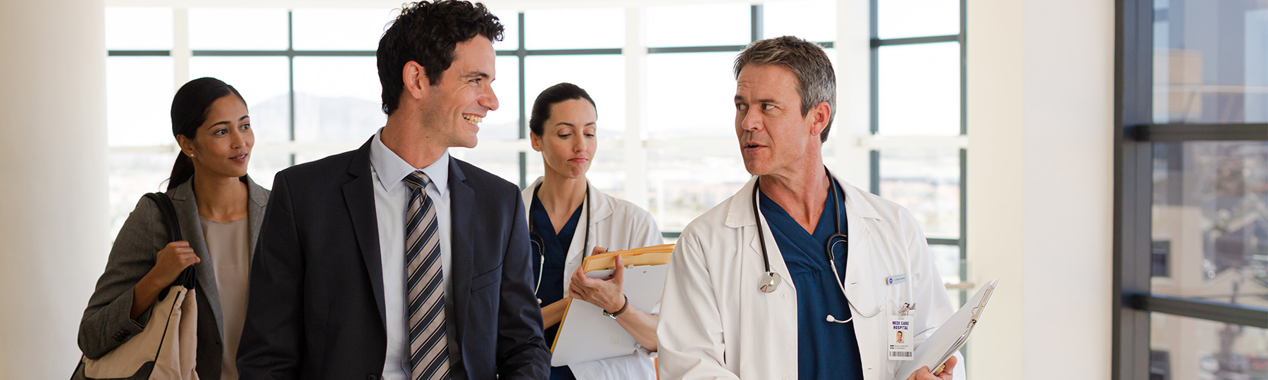 A doctor and business professional walk in the hallway discussing business.