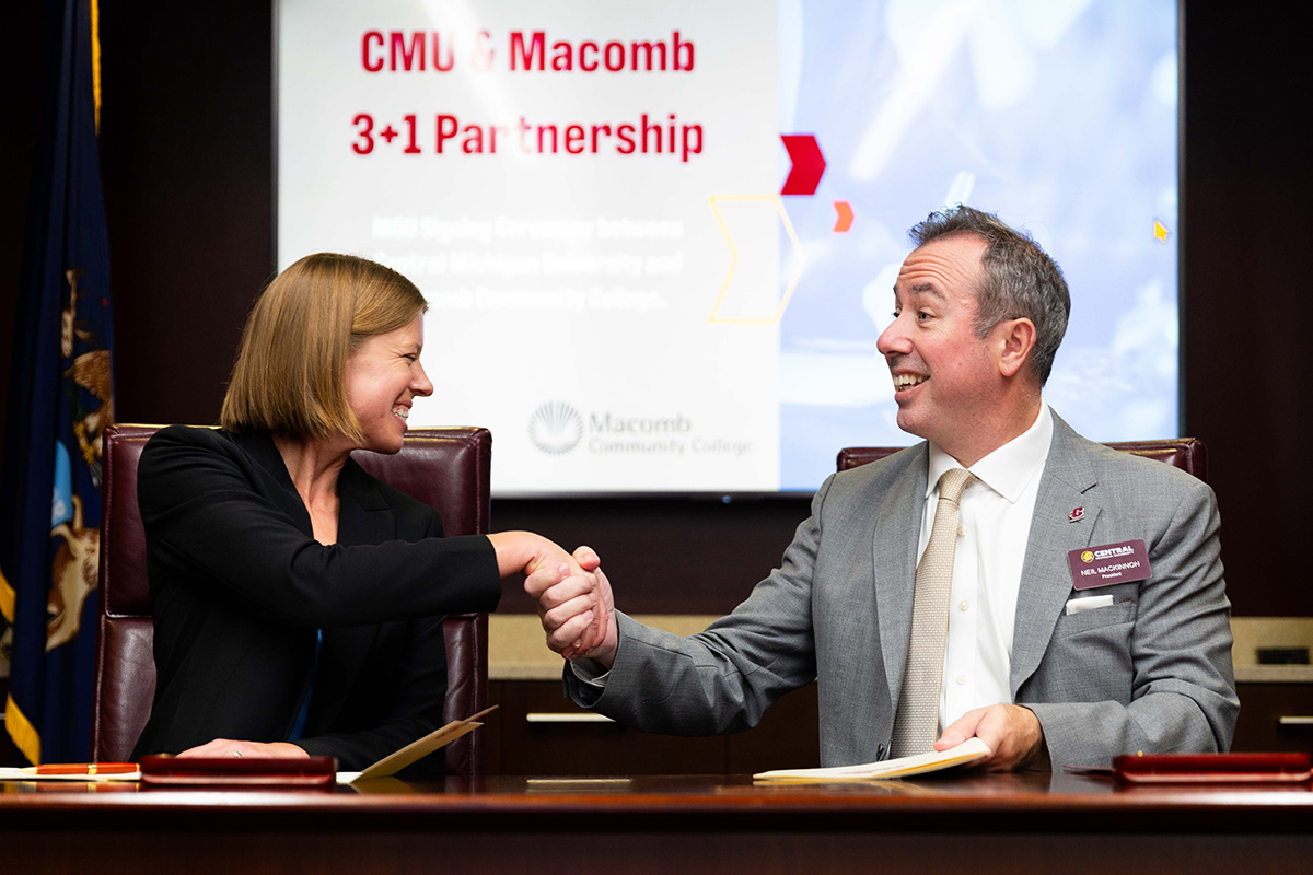 news-inline-20261013-02-macomb-3-1 President Lori M. Gonko of Macomb Community College and President Neil Mackinnon of CMU shake hands after signing a partnership document. They're sitting in front of a screen reading