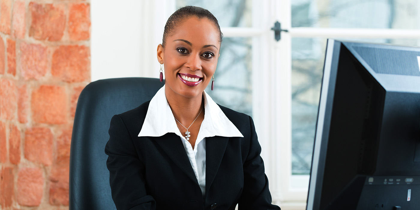 A paralegal in a blazer and collared shirt sits at a computer.