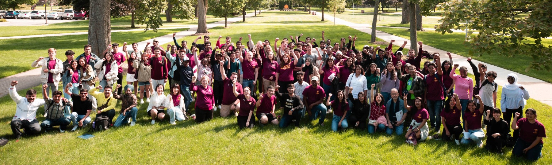 A large crowd of international students and supporters stand outside in an arch for a group photo