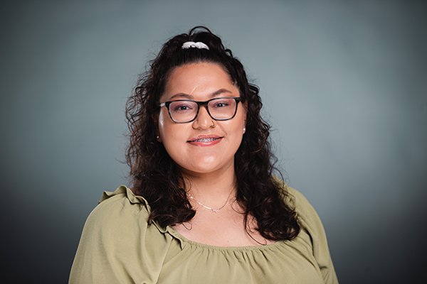Professional headshot of a smiling Cassandra Flores wearing a yellow shirt against a light grey backgound.