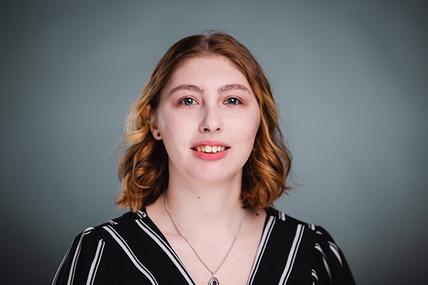 Professional headshot of a smiling Ginna Suttorp wearing a black and white striped shirt against a light grey backgound.