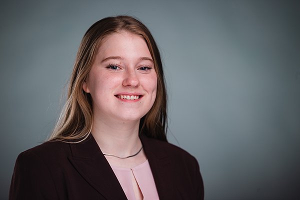 Professional headshot of a smiling Natalie Stetler wearing a black jacket and peach blouse against a light grey backgound.