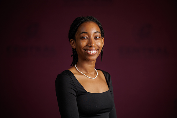 Professional headshot of Lillie Spates wearing a black top on a maroon background.