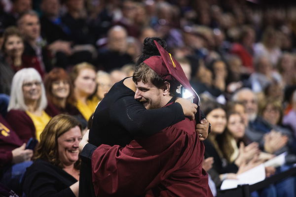 Male graduate hugs family member in commencement crowd