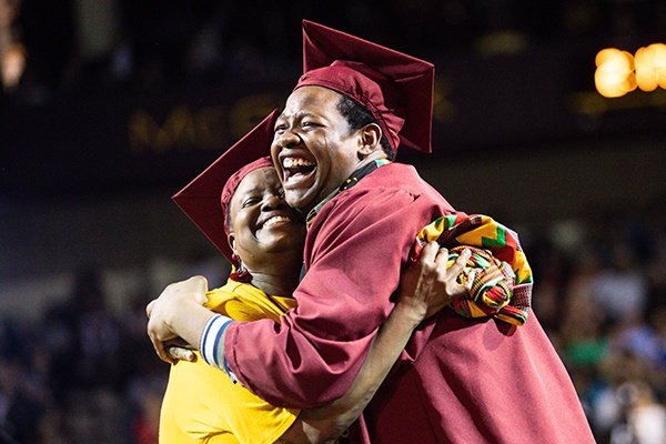 two students with their graduation caps on smiling and hugging
