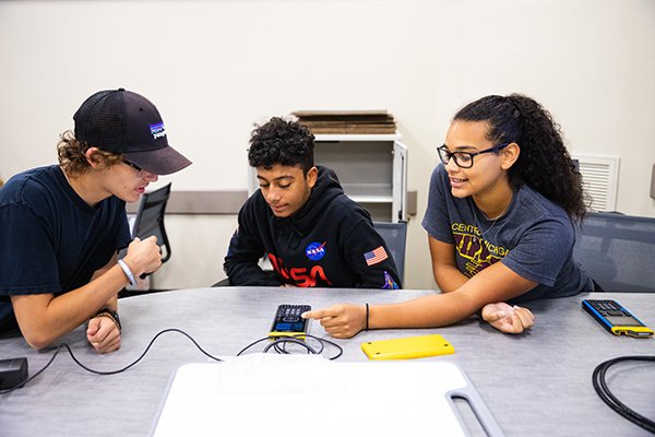 Three students sitting at a table in class working on a scientific calculator