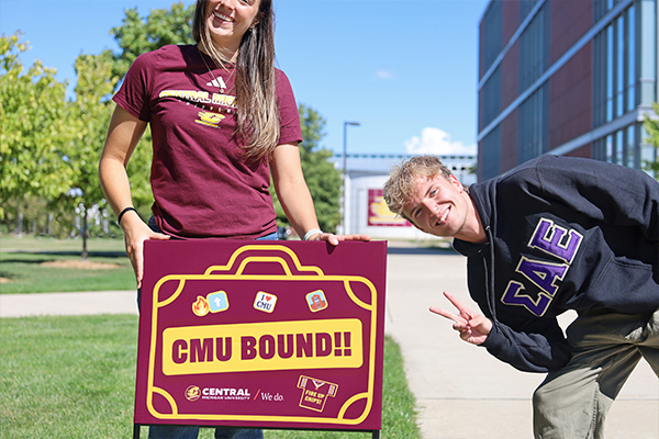 Two individuals stand next to a CMU Bound yard sign outside of Biosciences.