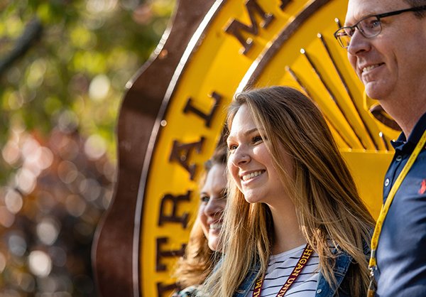 Student stands with family at CMU Seal, smiling.