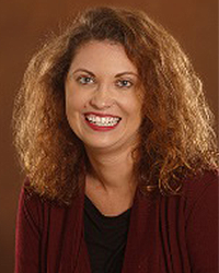 Ashleigh Laabs is an Alumni Board member who holds Emeritus Status and she is wearing a maroon shawl over a black top and has shoulder-length wavy brown hair.
