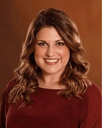Danielle Leone is an Alumni Board member who holds Emeritus status and she has shoulder-length brown hair and is wearing a dark red top.