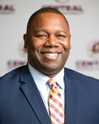 Headshot of Alumni Board of Directors Member Matt Franklin wearing a navy suit with a maroon and gold plaid tie and he is smiling with teeth while standing in front of a CMU backdrop.