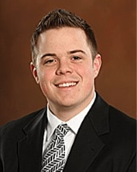 Greg Marx is an Alumni Board member and is an Emeritus member and he is wearing a black suit jacket and black and white tie and has short brown hair.