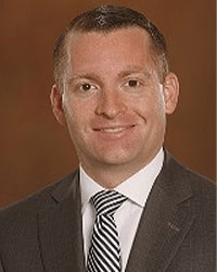 Jeffrey Stoutenburg is an Alumni Board member who holds Emeritus status and is wearing a gray suit with a navy and white striped tie and he has short brown hair.
