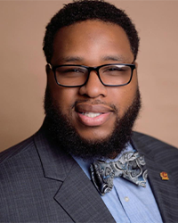 This is a headshot of Jonathan Glenn wearing a gray suit, blue undershirt, and bowtie.