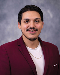 Headshot of Alumni Association Board of Directors member Kevin Bautista-Mancilla wearing a maroon blazer over a white under shirt. He has short black hair and is smiling with teeth.