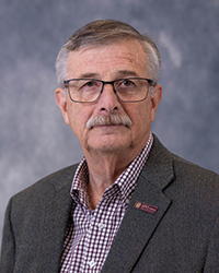 Kevin Campbell is an Alumni Board member who holds Emeritus status and he is wearing a gray suit jacket and plaid shirt. He has short hair.