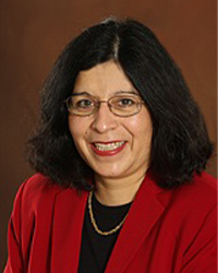 Laura Gonzales is an Alumni Board member who holds Emeritus status and she is wearing a red blazer with a black top underneath and she has shoulder length black hair.