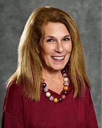 Linda Leahy is an Alumni Board member who is wearing a dark red top and a beaded necklace and she has long blonde hair.