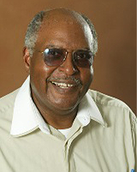 Raymond Jones is an Alumni Board member who holds Emeritus status and he is wearing a light green shirt and sunglasses and has gray hair and a mustache.