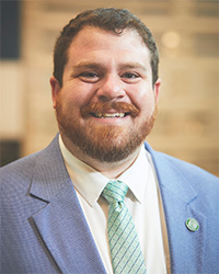 Spencer is wearing a green tie and a blue suit jacket over a white button up.