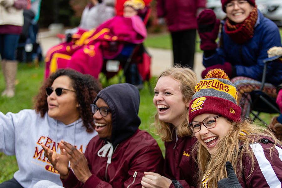 A group of student dressed in CMU apparel while sitting on the ground and cheering.
