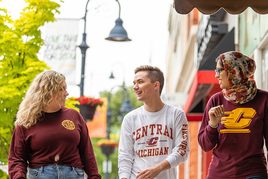Three Central Michigan University students wearing CMU apparel and walking.