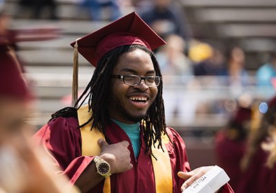 A graduating student at the graduation ceremony smiling in his cap and gown.