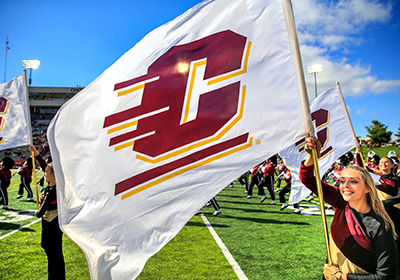 A student waving a white Central Michigan University flag with a maroon and gold action C in the center.