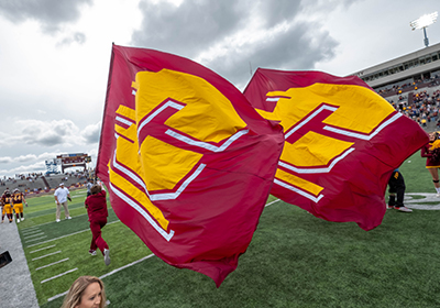 Two people running large Central Michigan University Maroon flags down the football field.