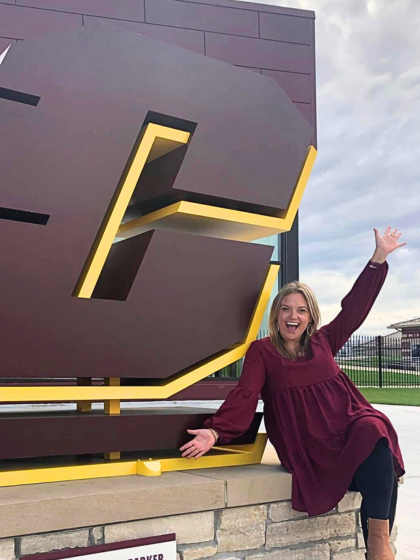 A woman poses for a picture next to a statue of the letter C.