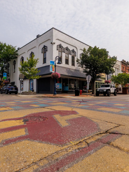 A low-angle view of a downtown Mount Pleasant street corner, showing a large maroon and gold Central Michigan University Action C painted on the intersection.