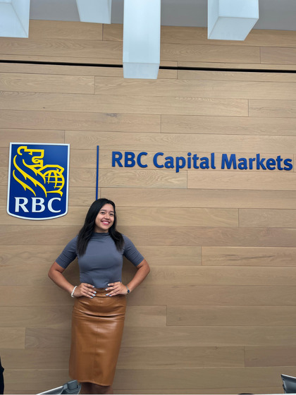 A woman in professional attire poses in front of a wooden wall with the RBC Capital Markets logo.