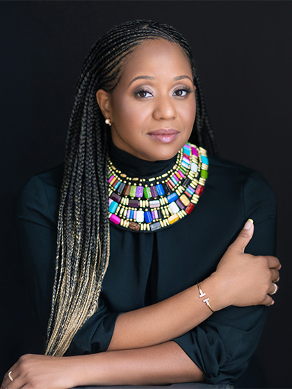 A profile photo of a woman in a black shirt with braided hair and a large necklace.