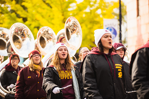 The Central Michigan University band playing music while walking down a street.