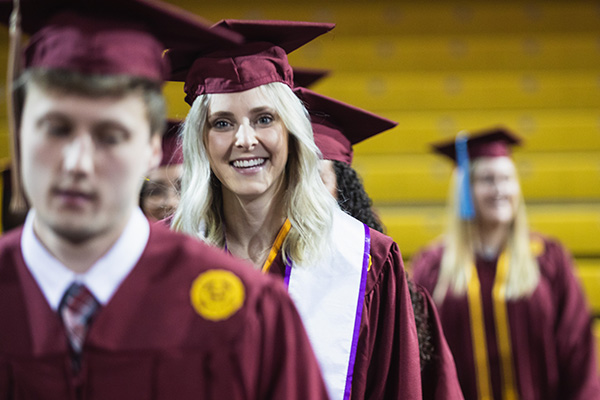 A student wearing a cap and gown and smiling at the camera during graduation.