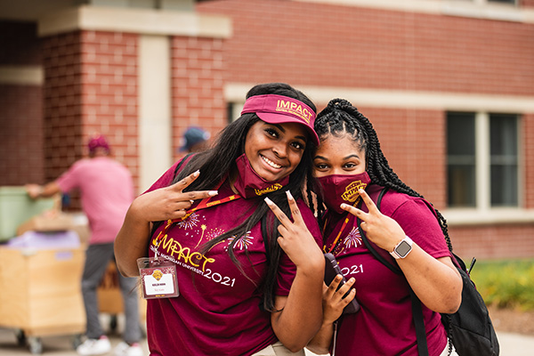 Two students dressed in CMU apparel at IMPACT 2021 making peace signs in front of the camera.